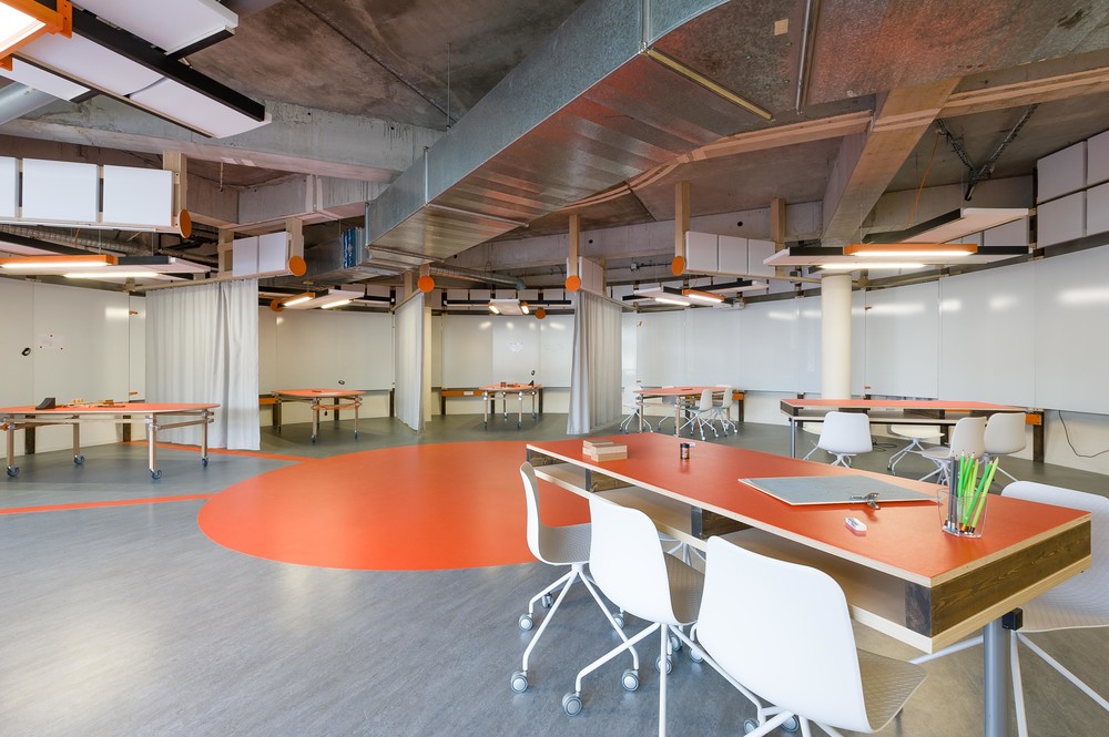 Un arc de cercle composé de panneaux blancs Veleda, scandé par des luminaires acoustiques délimite les studios de création. Ils sont aménagés d’une table sur mesure et de chaises de réemploi.